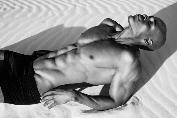 A guy with a gorgeous abs is lying on the sand