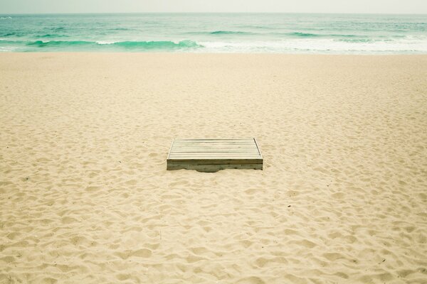 Caja en la arena amarilla de la playa. Ondas turquesas