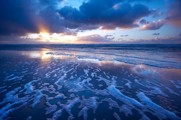 Les vagues moussaient du surf au coucher du soleil gris-mauve