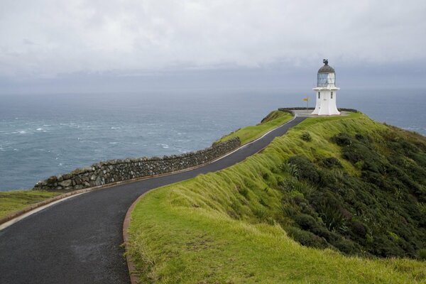 The road to the lighthouse on the cape with green slopes