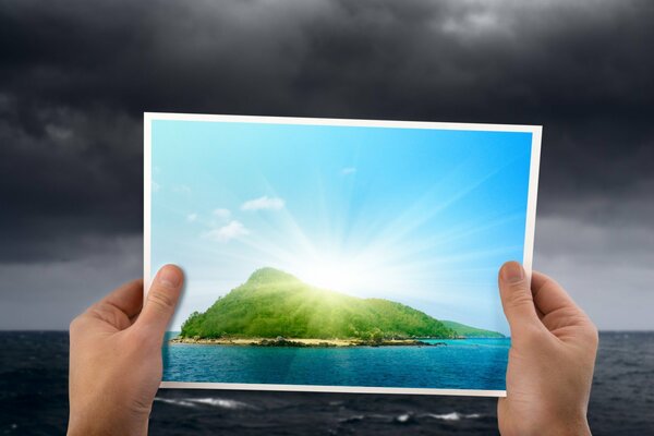 Hands holding a photo of the island against the background of a thunderstorm