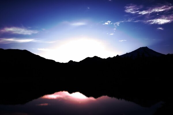 Schwarze Berge und die Sonne spiegeln sich im Wasser wider