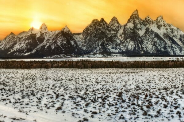 Felsen im Schnee auf dem Hintergrund des orangefarbenen Himmels