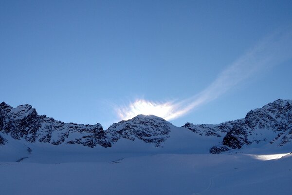 The sun comes out from behind the snowy mountains