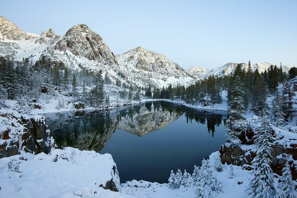 Paesaggio invernale: lago, cielo, montagne e foresta nei toni del blu e bianco