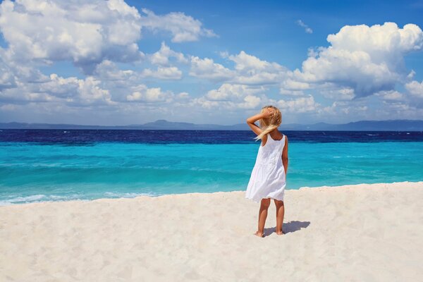 Bild eines Mädchens in einem weißen Kleid am Strand in der Nähe des blauen Meeres