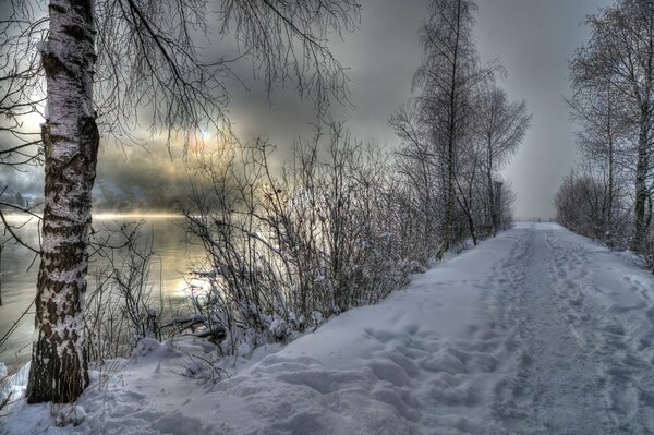 Snow-covered road by the river at sunset