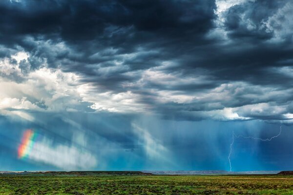 A rainbow peeps through clouds and lightning