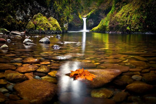 Ein steiniger See mit einem kleinen Wasserfall im Herbst