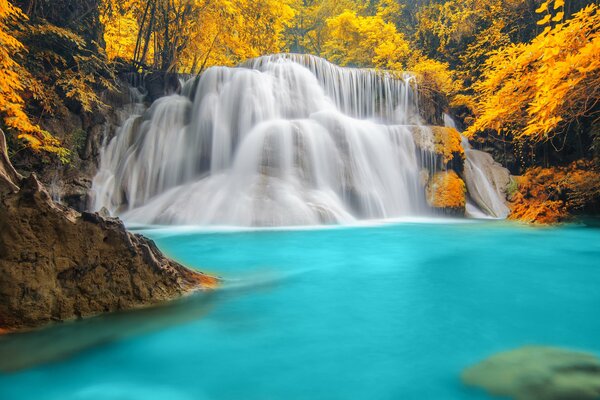 Autumn landscape of a waterfall on a blue lake surrounded by a yellow forest