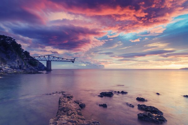 Bruchstücke einer Brücke im Meer in der Farbe eines rosa Sonnenuntergangshimmels