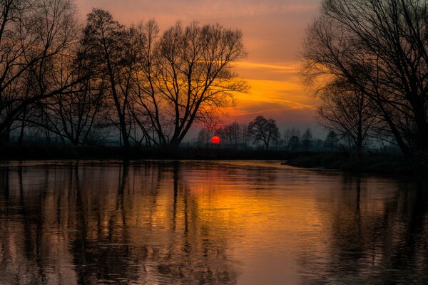 A fiery sunset is reflected in the river