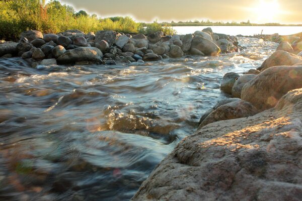 Стремительный поток воды сквозь камни к солнцу. Фото речки