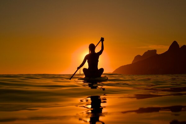 Silhouette of a girl in the sunset rays on a kayak