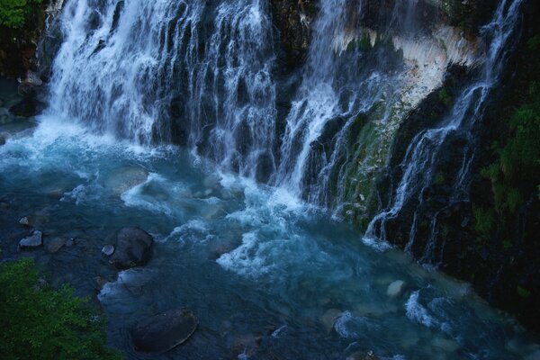 Felsiges Ufer unter einem Wasserfall in der Dämmerung