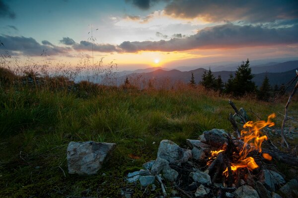 Das Feuer wurde vor dem Hintergrund einer schönen Berglandschaft mit Nadelbäumen vor dem Hintergrund der Sonnenuntergang entzündet