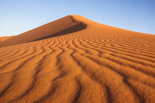 Deserto con motivo sulla sabbia a forma di linee ondulate su uno sfondo di cielo blu