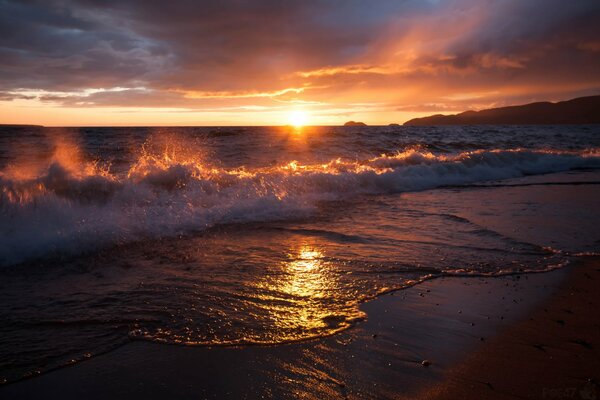 Beau coucher de soleil sur le fond des vagues qui se précipitent sur le rivage sablonneux