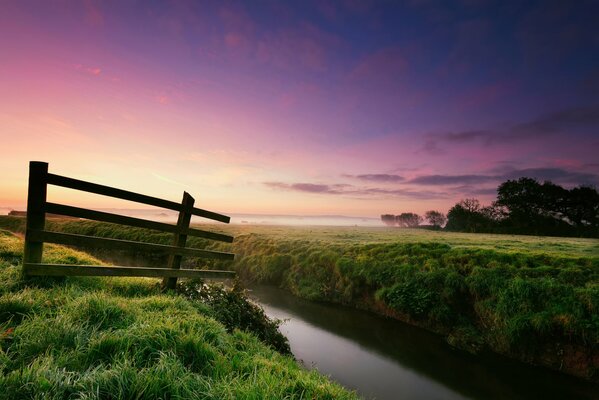 There is a fence near the river on wet dew