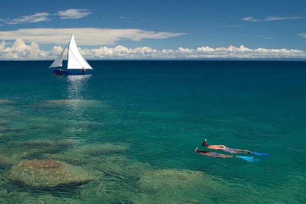 A couple swimming underwater to a boat