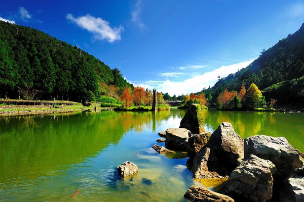 Belle vue sur l eau avec des pierres qui en saillie, un ciel bleu et des arbres rouges au loin