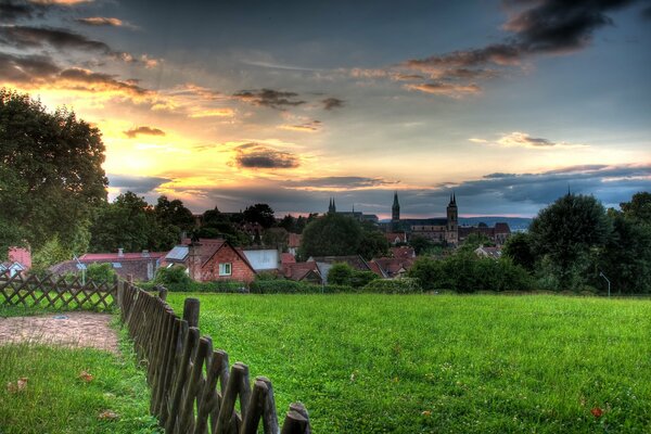 Behind a green field, a small village under the sky during sunset