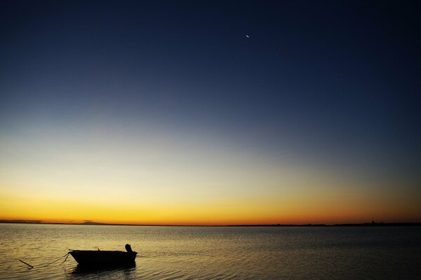 Barca solitaria in mare, sullo sfondo del cielo al tramonto