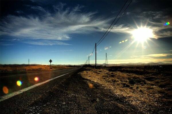 A prairie road. The sun. There are many pillars along the road