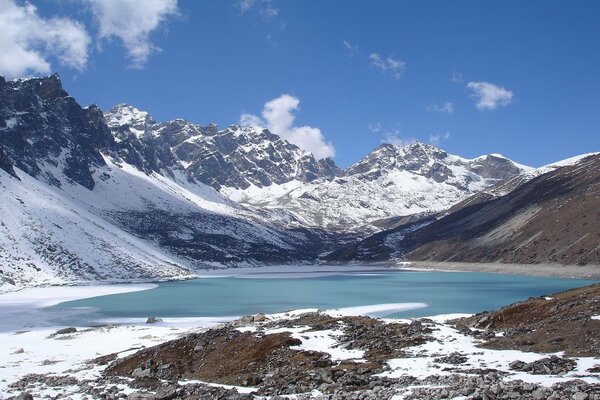 Lago de montaña con borde de hielo entre picos de montaña cubiertos de nieve