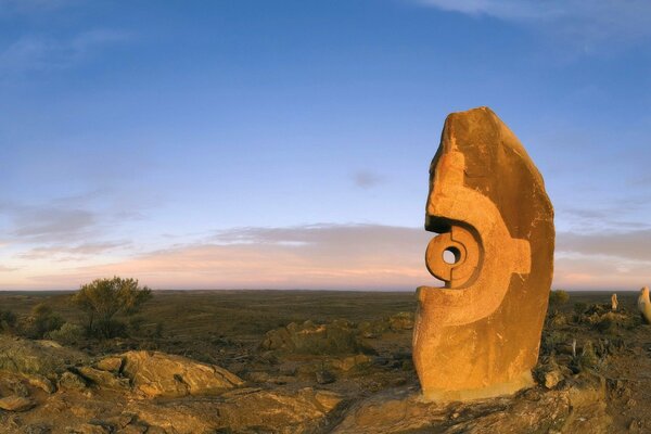 Mysterious stone sculpture on the background of a green plain