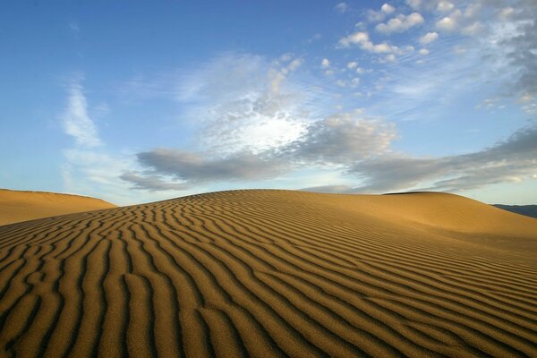 Waves of desert hill sand under light feather clouds