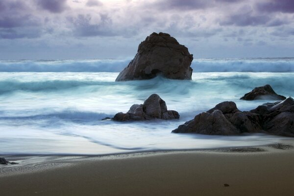 Les vagues de mousse se brisent sur les rochers sous le ciel orageux