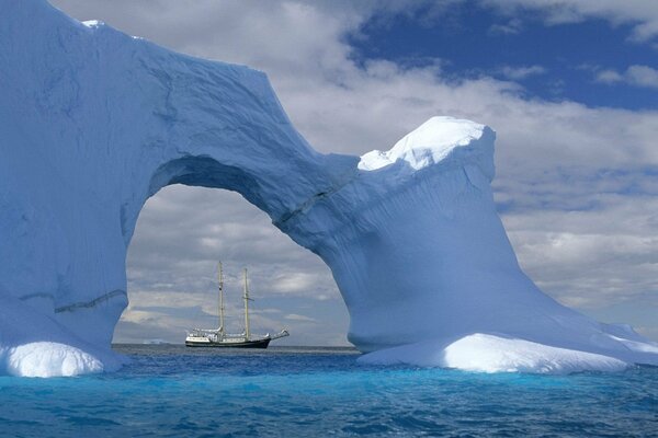 Voilier blanc sur les vagues derrière un iceberg