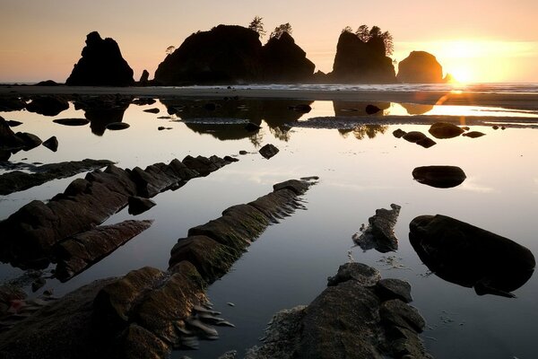 Il sole sorge da dietro le rocce sopra l acqua