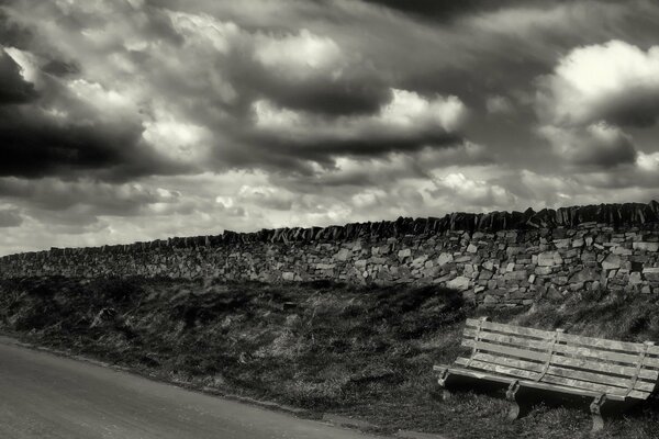 A bench by the road and a brick wall. Black and white photo