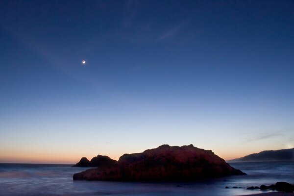 Rocher dans la mer au coucher du soleil au clair de lune