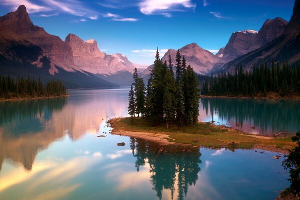 An island with tall trees surrounded by a water surface on the background of mountain ranges