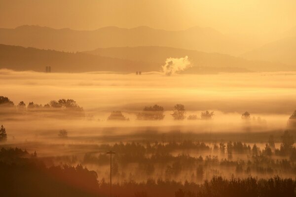 A sleeping village is visible in the morning fog