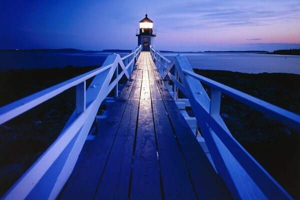 Ein Leuchtturm im Abendlicht am Ende einer Holzbrücke