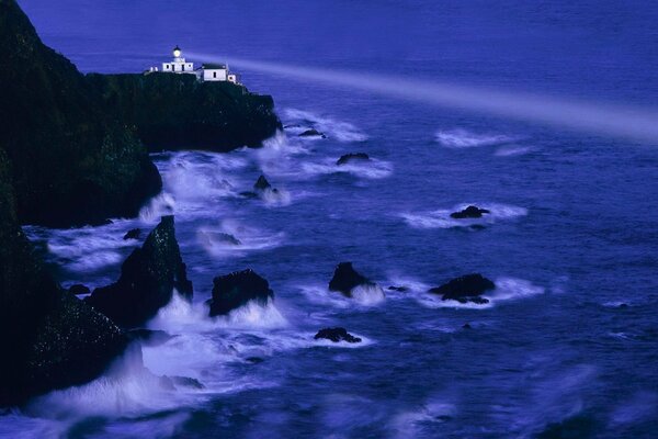 El rayo del faro en el fondo de las olas que golpean las rocas