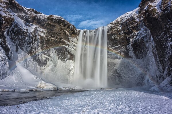 Cascada entre la nieve y las montañas en Islandia