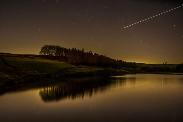 Shooting star on the background of the night sky by the lake and forest