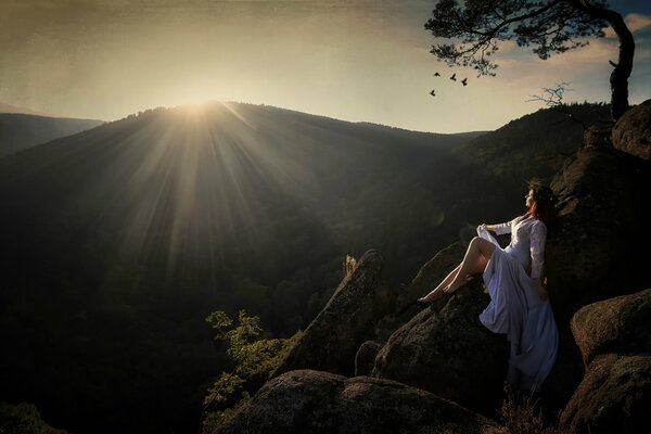 Fille sur les rochers dans les montagnes sur fond de soleil couchant