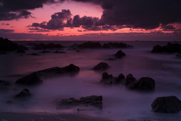 Coucher de soleil rose dans le brouillard marin parmi les pierres