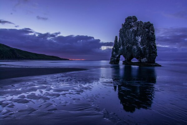 A gray block of rock on the shore, against the background of a lilac sky