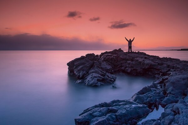 Homme sur la plage rocheuse de la mer au coucher du soleil