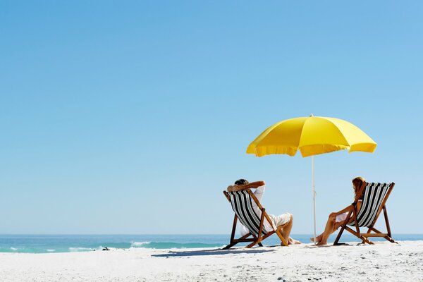 Zwei Personen sitzen in Liegestühlen am Strand