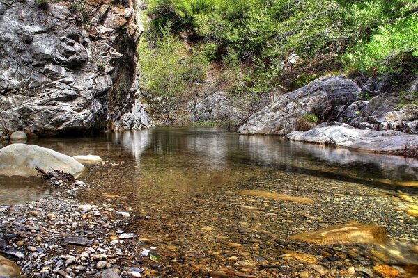 Чистейшая вода с галькой на фоне высоких скал