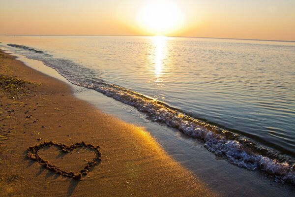 A heart on the sand against the background of a sea sunset