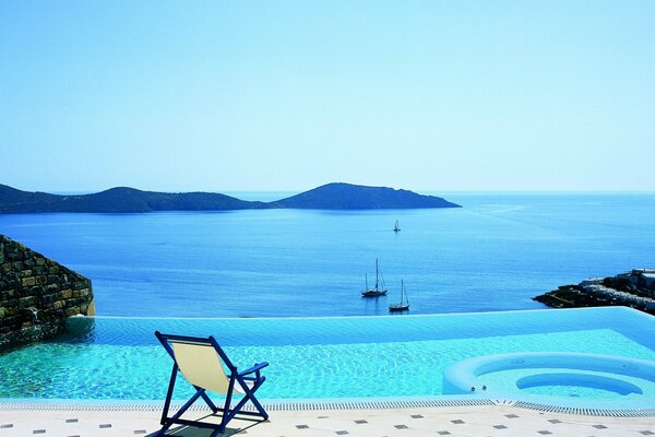 Der Sessel am azurblauen Pool liegt am Meer, wo die Yachten laufen und die Berge sichtbar sind und das Meer selbst mit dem Himmel verschmilzt